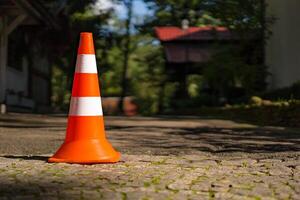 a rayas el plastico la carretera firmar para estacionamiento en el pavimento en el borroso antecedentes. naranja tráfico la carretera cono con dos blanco rayas. de cerca foto