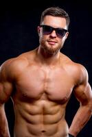 Muscular guy with naked torso posing with hands on waist. studio photo. Portrait of a handsome man with naked torso in sunglasses. photo