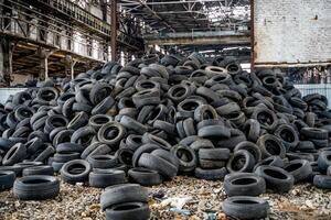 Big pile of automobile tires on the broken-down plant. Many black rubber tyres on the ground inside the old huge empty building. photo