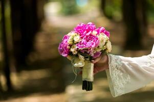 boda. el novia en un vestir en pie en un verde jardín y participación un ramo de flores foto