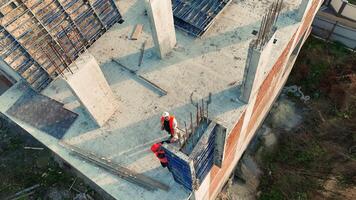 aéreo ver construcción trabajadores en edificio sitio, aéreo ver de construcción trabajadores colaborando en un hormigón estructura a un edificio sitio. video