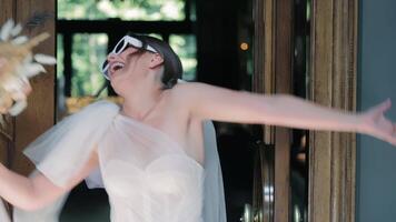 brud med eleganta solglasögon poserar, lekfull brud bär trendig solglasögon, innehav bukett på de dörröppning. video