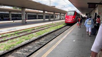 Roma, Italia 29.10.2023 viaggiatori in attesa arrivo di si avvicina treno, i viaggiatori con bagaglio in attesa come un' rosso alta velocità treno approcci il stazione piattaforma. video