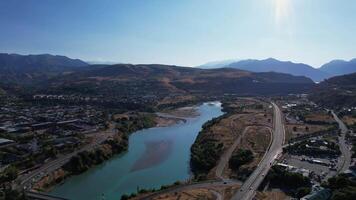 The drone flies over the highway neat to the mountain lake. Sunny summer day. There are hills covered with greenery all around. video