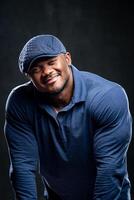 Smiling african american man posing. Attractive male with muscular body type in stylish and fashionable blue shirt and hat. photo