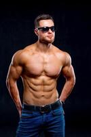 Sexual muscular man posing over dark background. Muscular body and strong abs. Looking at side. Studio shot. photo