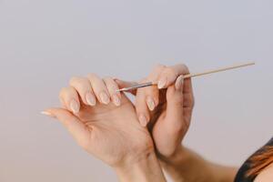 mujer con bien arreglado manos cubre su uñas por barniz de gel utilizando un Delgado cepillo en un blanco antecedentes. de cerca foto