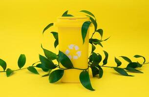 Yellow recycling bin embellished with fresh green leaves is set against yellow background. photo