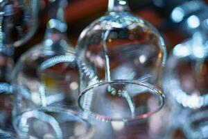 a wide transparent wine glass hangs on the background of other wine glasses in the bar. Close-up photo