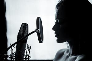 joven mujer con el micrófono en el grabación estudio. profesional vocal grabación. negro y blanco sesión de fotos. hermosa niña cantante. retrato. de cerca. foto