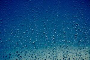 raindrops flow down the window of a house on the background of a blue sky. Close-up photo