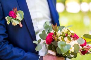 hermosa ramo de flores de mezclado flores en el manos de un novio en azul traje. Boda manojo de Fresco flores para novia y un pequeño linda flor en el ojal clavado a un Boda traje en novio. foto