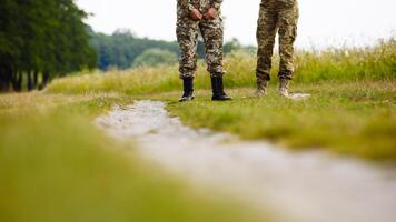 ver de el piernas de dos hombres en militar uniformes en botas cerca el ruta en el campo foto