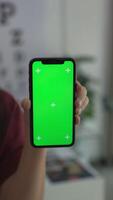 Hand holding phone green screen vertical in office, smartphone green screen video