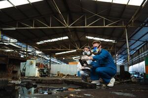 A team of engineers wearing safety suits and gas masks is under inspection of a chemical tank at an industrial site. photo