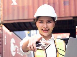 Female woman lady girl person people human white hardhat helmet safety look at camera happy smile pointing finger cheerful beautiful pretty container construction work job import export manufacturing photo