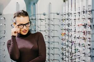 Woman with Eyeglasses in Optical Store - Beautiful girl wearing glasses in optician shop. Ophthalmology. photo