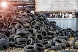 grande manojo de antiguo negro llantas desde diferente vehículos acostado en el abandonado planta. vertedero de usado coche ruedas en el arruinado fábrica antecedentes foto