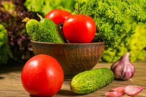 un lleno cuenco de vegetales. Tomates y pepinos en un de madera mesa. verde ensalada en el antecedentes. foto