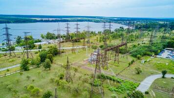 Electrical transmission lines over green farm fields near the river. Power lines in the beautiful landscape of nature. Aerial view photo