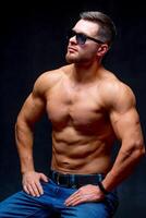 retrato de un atlético muscular barbado hombre posando en un negro antecedentes. masculino en lentes demostración músculos. foto