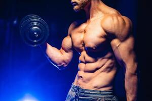 Handsome power athletic man bodybuilder doing exercises with dumbbell. Fitness muscular body on black and blue background. Fitness concept. photo