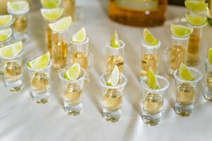 parte superior ver de vodka en corto lentes con Lima en el blanco Manteles. vodka, Ginebra, tequila en pequeño lentes con Lima o limón. foto