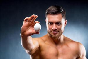 Handsome Man holding raw egg in hands showing to the camera. Attractive guy keeping healthy lifestyle. Closeup. photo
