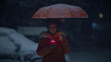 Young African Woman Standing on Street at Night During Snow Fall with Umbrella video