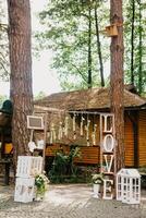 Beautiful white color outside decor for wedding ceremony in scenic place in old wood. White arch decorated with fresh flowers and rows of many wooden chairs at high pine trees background. photo