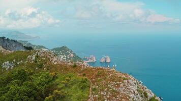 Hiker Overlooking Spectacular Seaside Cliffs Faraglioni in Capri, Italy. Woman walking on top of rock, gazing out over a stunning seascape dotted with boats. video