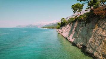 Cliffside längs en lugna hav, med skikten av geologisk historia. vegetation klamrar sig fast till klippig hällar ovan en avskild sten strand. antenn se av natur i sommar kroatien. video