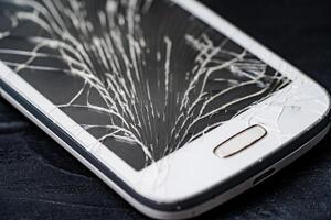 Close-up of a cracked touchscreen of a white phone. Broken screen glass of a smartphone on the black wooden background. photo