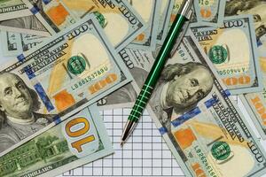 hundred-dollar bills are scattered on the table lie with green pen. Close-up photo