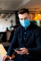 Man in mask working in phone during quarantine. Stylish man sitiing in social media on quarantine. photo