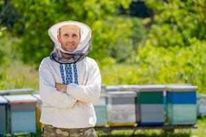 Beekeeper in protective workwear. Hives background at apiary. Works on the apiaries in the spring. photo