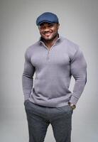 Smiling positive guy standing with hands in pockets. Attractive affrican american man in comfotable gray suit cap and jeans. photo