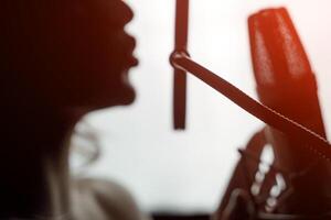 Sexy silhouette female profile with pretty face and bare shoulder near microphone on studio background. Side view portrait of woman singing to microphone. Close-up photo