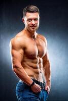 half turned model guy is posing to the camera in the dark grey background. Half waist photo. Strong muscular body. Closeup. photo