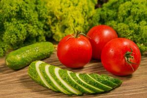 Fresco vegetales. Tomates y pepinos en un de madera mesa. verde ensalada en el antecedentes. sano comida, dieta concepto foto