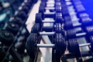 Many dumbbells are at stand at the modern sport gym. View of rows of dumbbells on a rack in a gym. photo