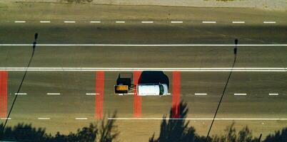 a car with a trailer drives along a highway with red marked lines. Aerial view photo