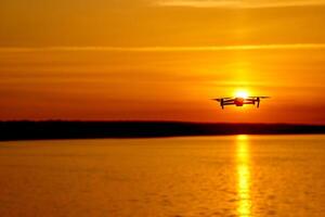 Modern technological background - silhouette of flying drone in glowing red sunset sky. Elements of this image furnished by NASA photo