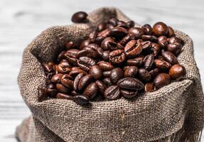 Close-up of dark fresh aroma beans in a small sack. Full bag with roasted coffee grains over the blurred background. photo