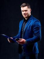 Confident businessman holding a phone and a folder in hands. isolated over black background in studio. photo