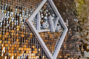 decorated wall in the form of gold squares and with a white inscription in a rhombus is at the wedding in the cafe. Close-up photo