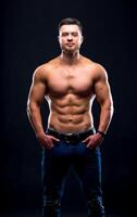 Muscular guy with naked torso posing with hands in pockets. studio photo. Portrait of a handsome man in jeans. photo