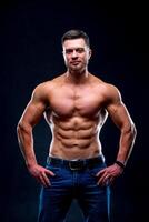 Muscular guy with naked torso posing with hands on waist. studio photo. Portrait of a handsome man in jeans. Closeup. photo