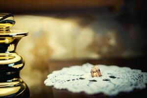 Luxury wedding rings on vintage knitted napkin over the blurred background. White napkin with two golden rings with precious pebbles on the table. photo