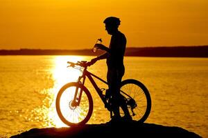 silueta de un ciclista con puesta de sol antecedentes. naranja cielo, pasatiempo, sano hábitos. Bebiendo agua mientras descansando foto